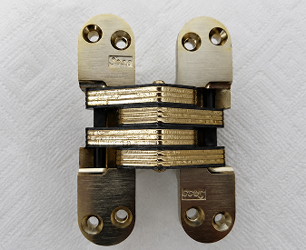Close-up of a SOSS invisible hinge showing stacked metal plates and countersunk mounting holes.