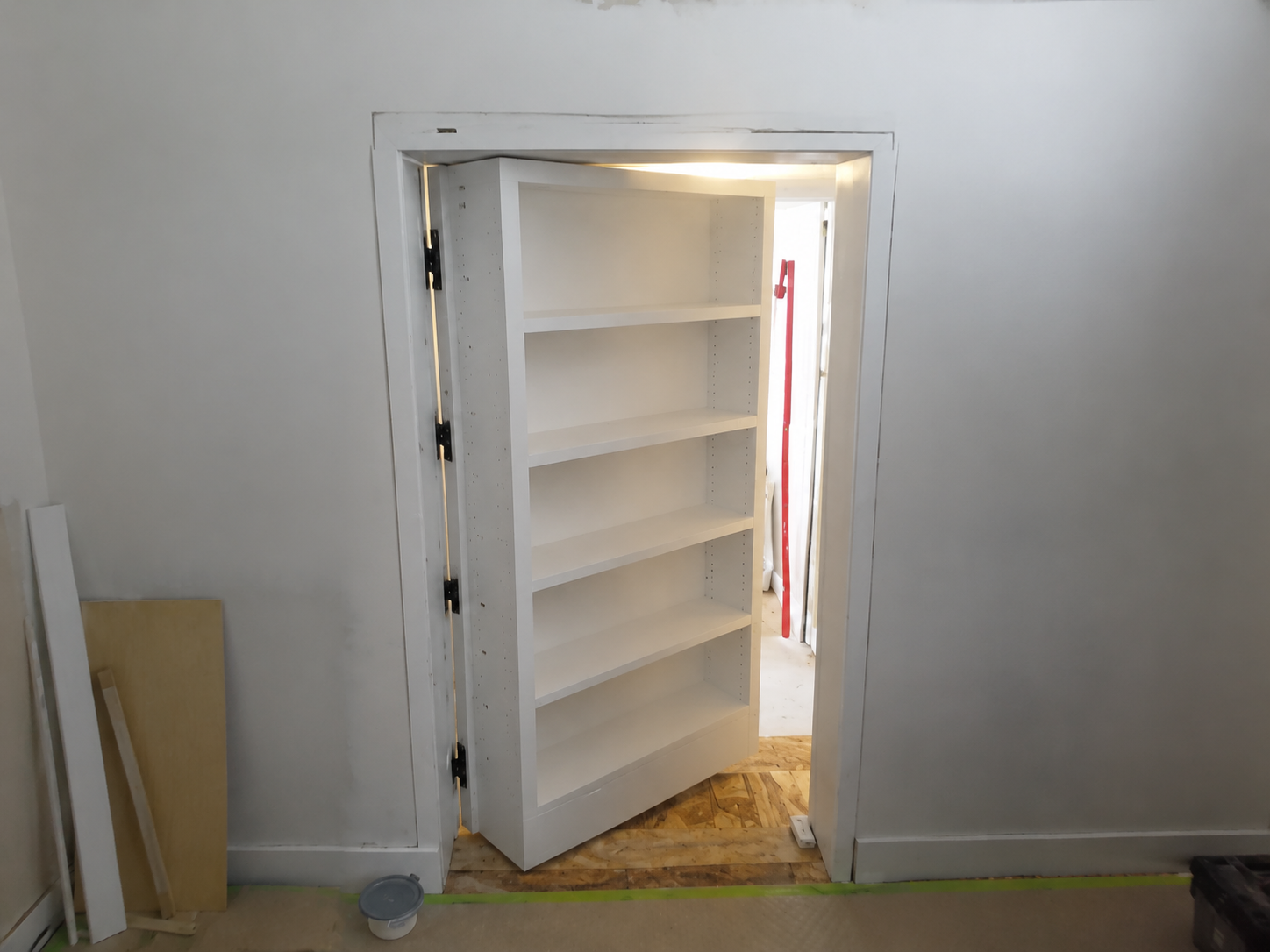 White hidden bookcase door opened to reveal a concealed storage room during installation.