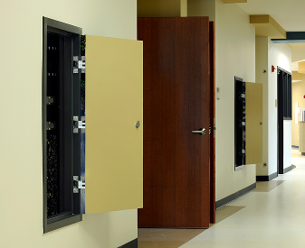 Open utility wall panels and a wood door along a commercial hallway.