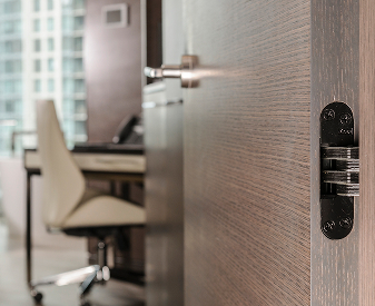 SOSS invisible hinge installed on a wood office door with a modern workspace in the background.