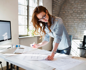 Architect reviewing building plans at a drafting table in a modern office.
