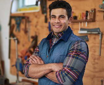 Contractor standing with arms crossed in a workshop with tools on the wall.