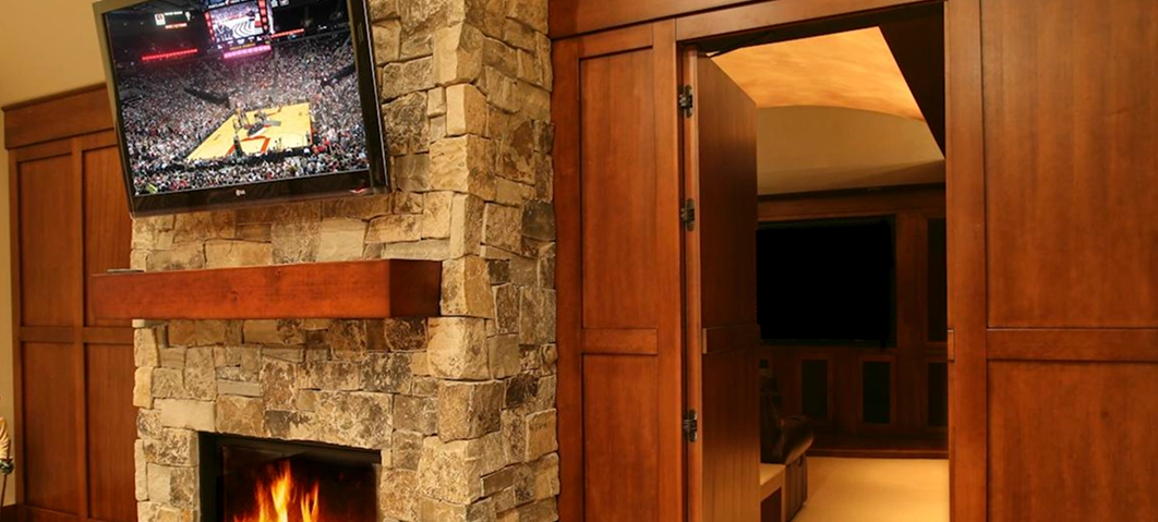 Hidden home theater entrance with wood panel doors beside a stone fireplace.