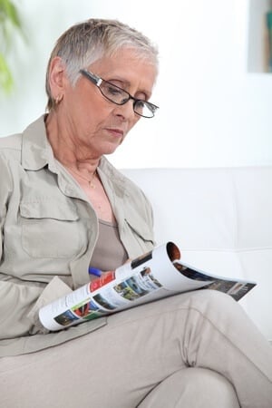 elderly woman sitting in chair with legs crossed reading magazine