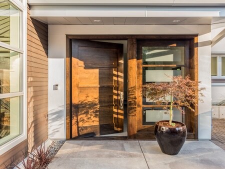 beautiful wood door as entrance to new luxury home: large and wide hardwood door with windows and potted plant to right of door in exterior of beautiful house. cement patio. door is slightly ajar